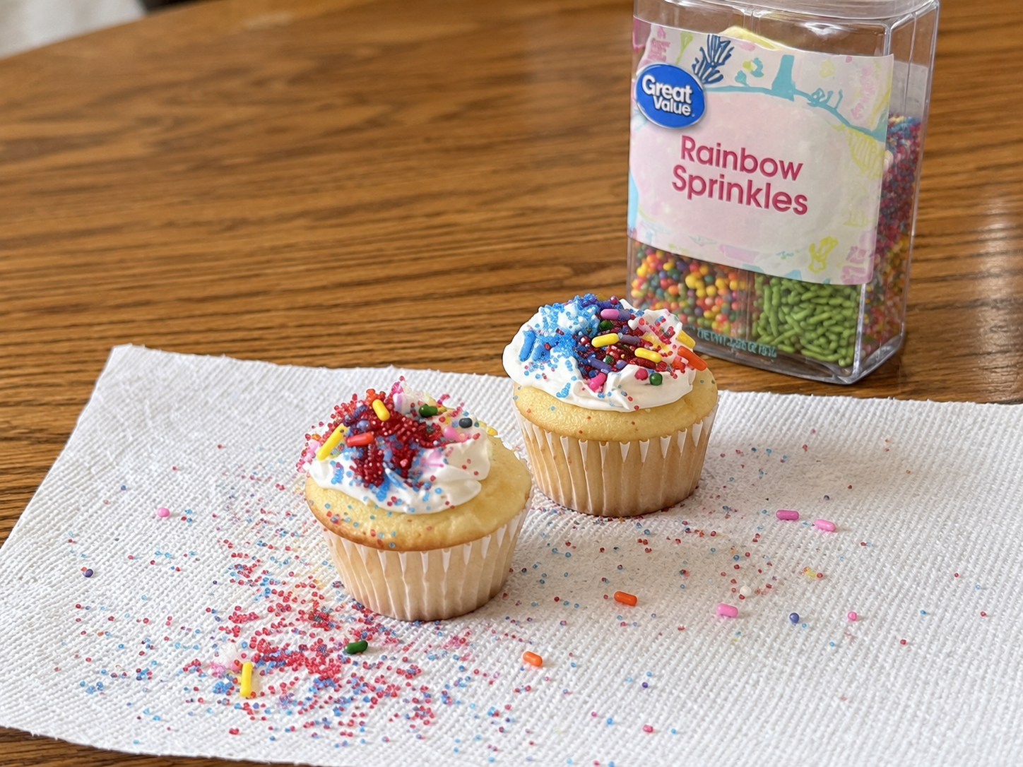 Two frosted mini cupcakes decorated with colorful sprinkles on the table