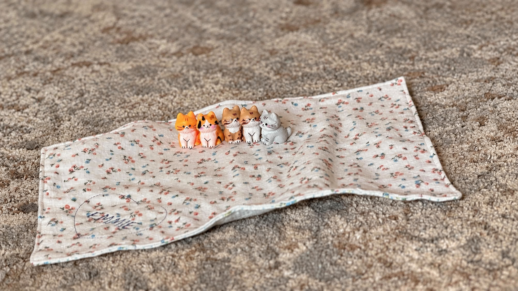 Five colorful miniature kitten figurines sitting together on a small floral blanket